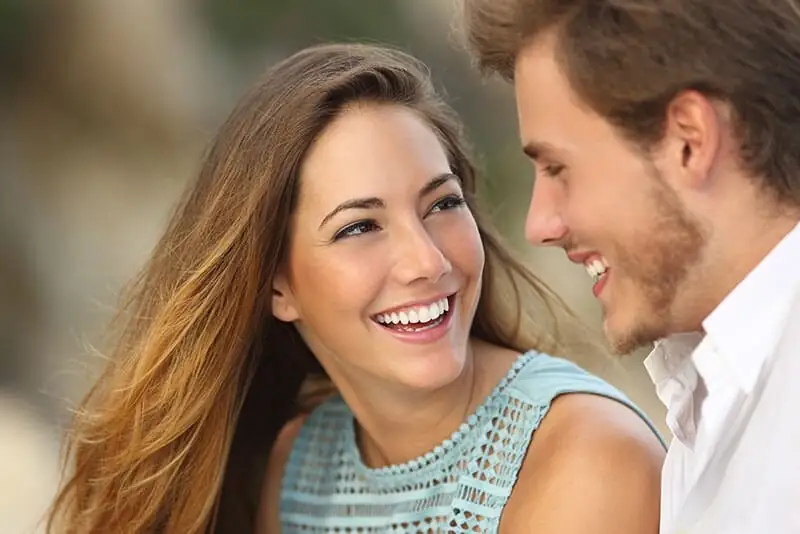 Two smiling adults looking at each other, showing their teeth.